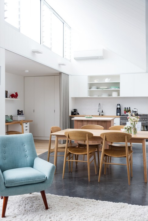 Modern open-plan kitchen and dining area with wooden table, blue armchair, and white cabinetry.