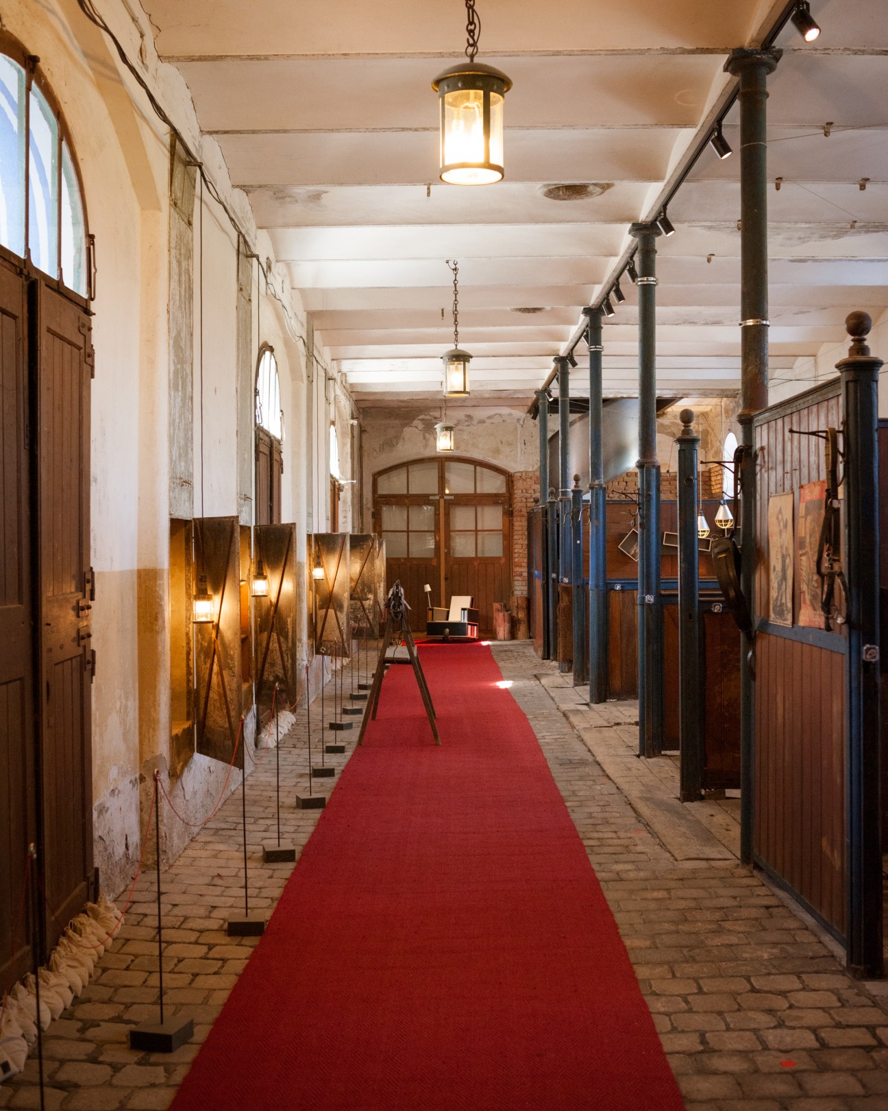 Interior corridor of Moormann showroom with red carpet, wooden stall doors, pendant lights, and black metal railings.