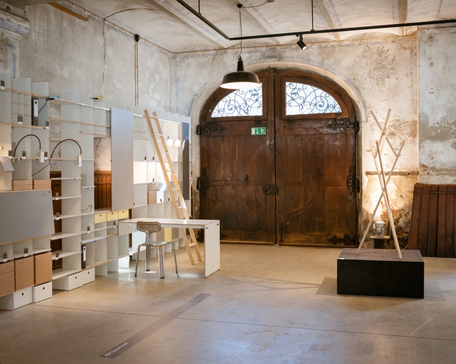 Interior of Moormann showroom with wooden and white shelving units, pendant lamp, and large wooden doors with ornate ironwork.