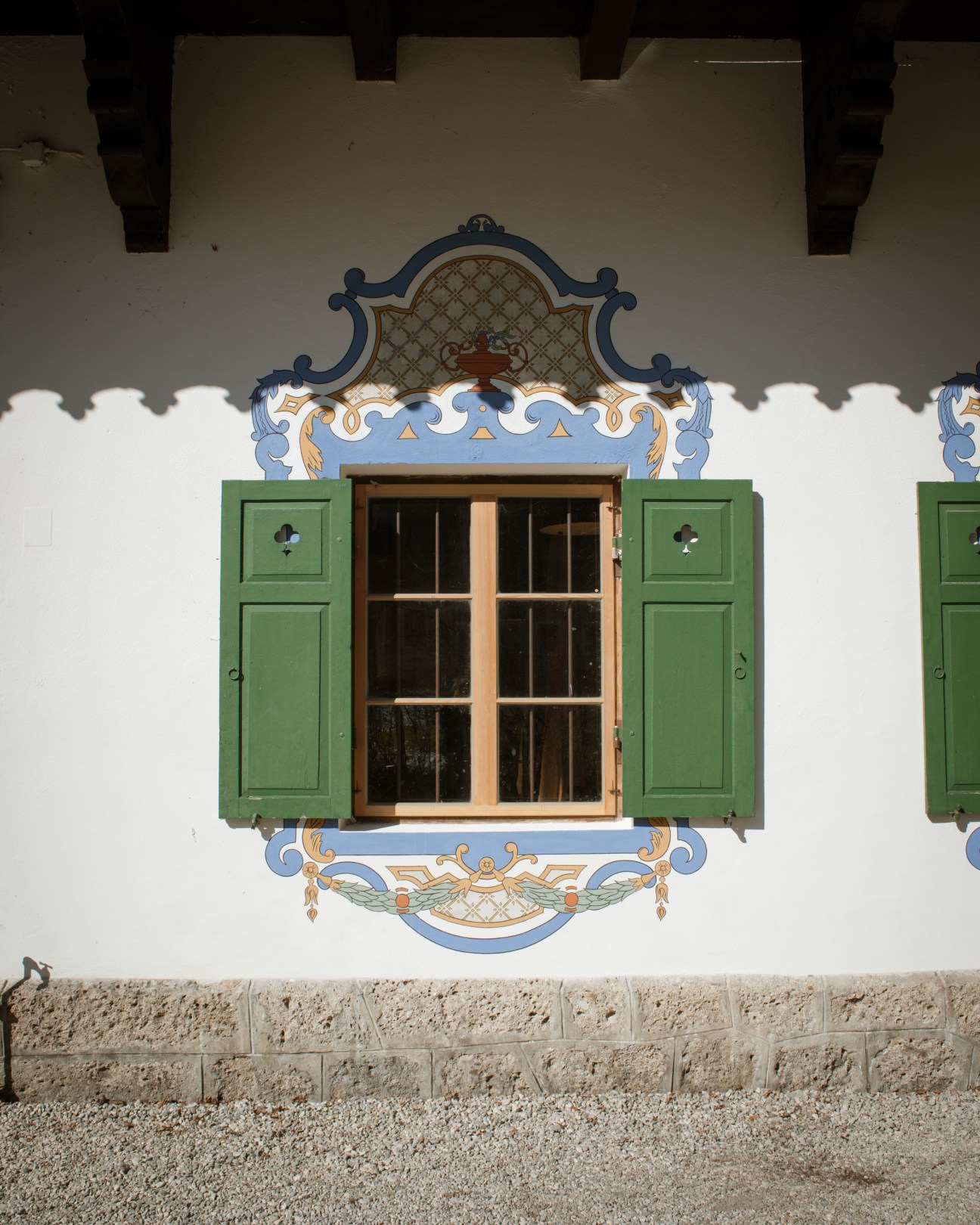 A white building facade with ornate blue and gold ceramic tile decoration surrounding a wooden-framed window with green shutters.