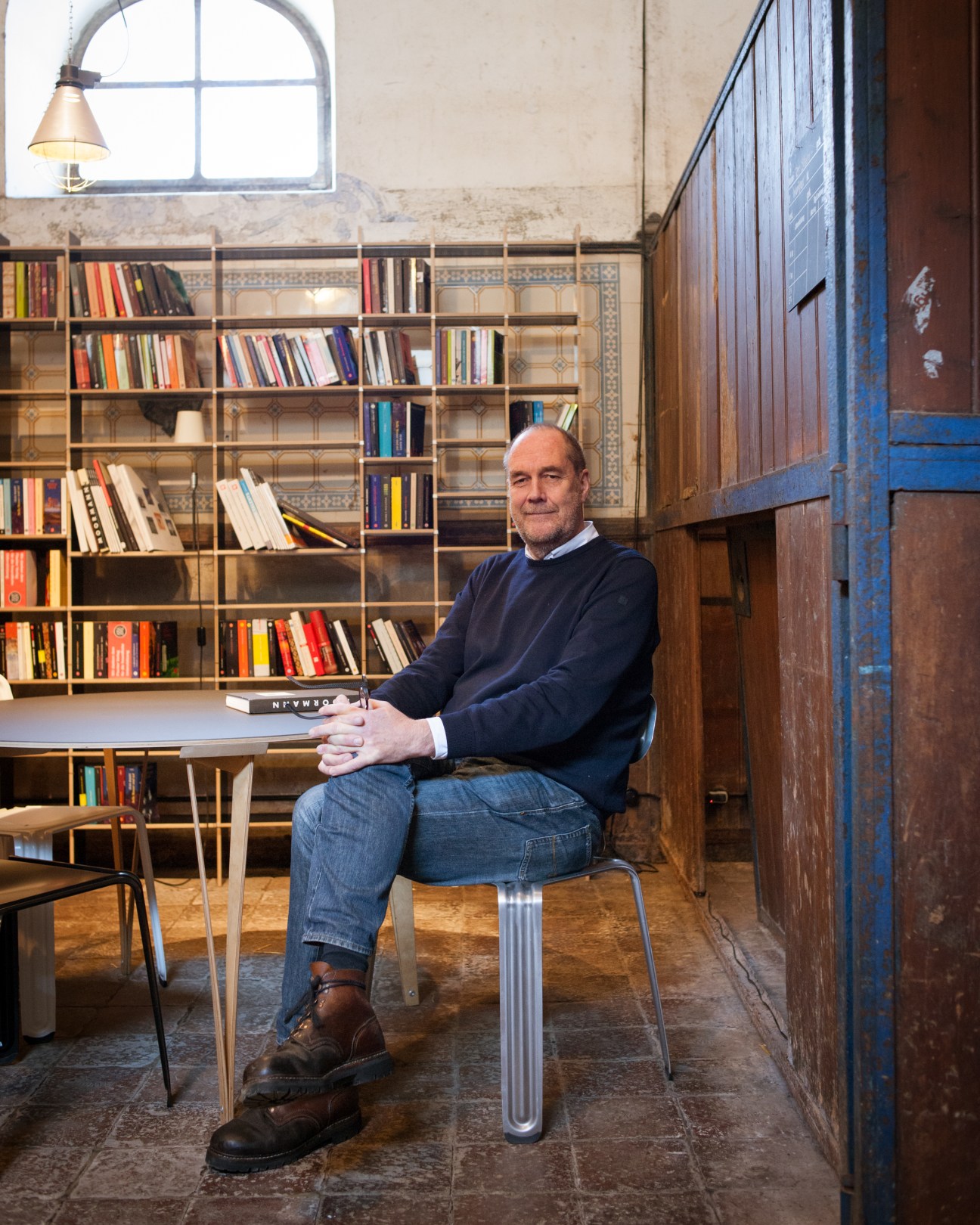 Nils Holger Moormann sits in his office surrounded by bookshelves and wooden furniture.