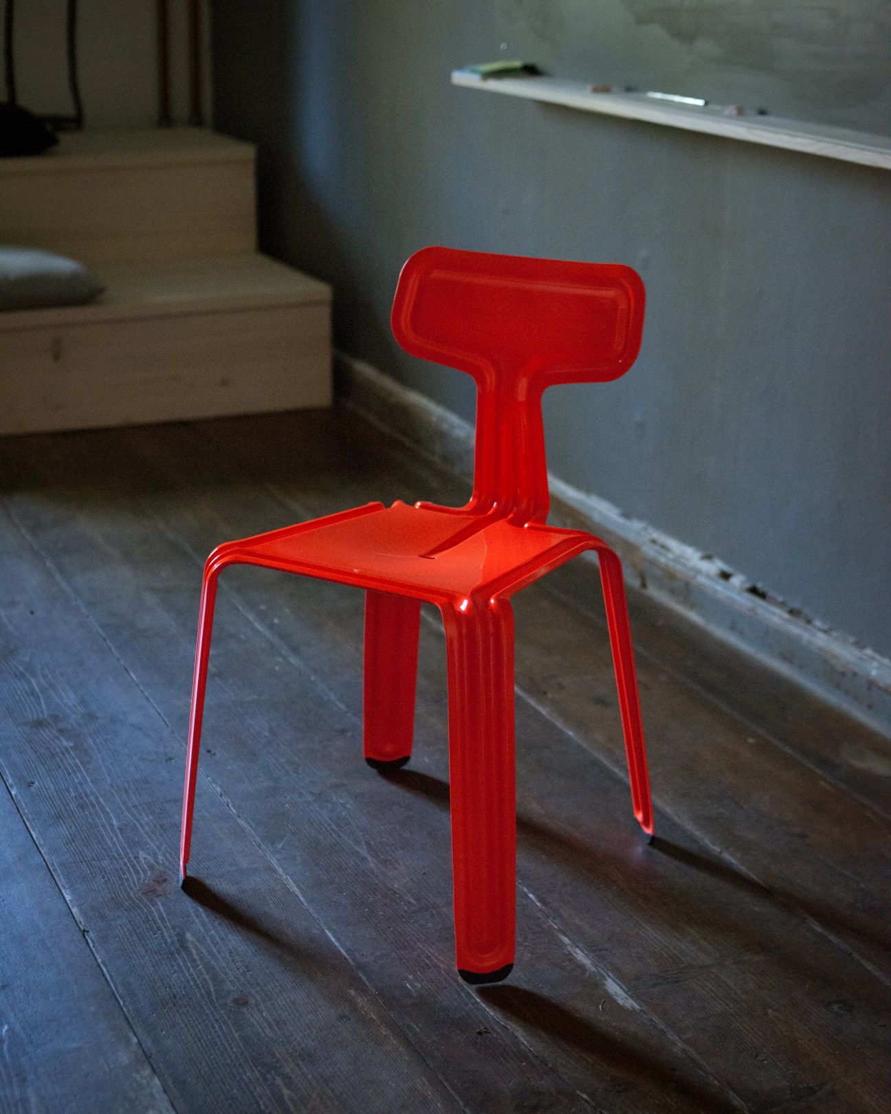Red plastic pressed chair displayed on dark wooden floor in minimalist interior.