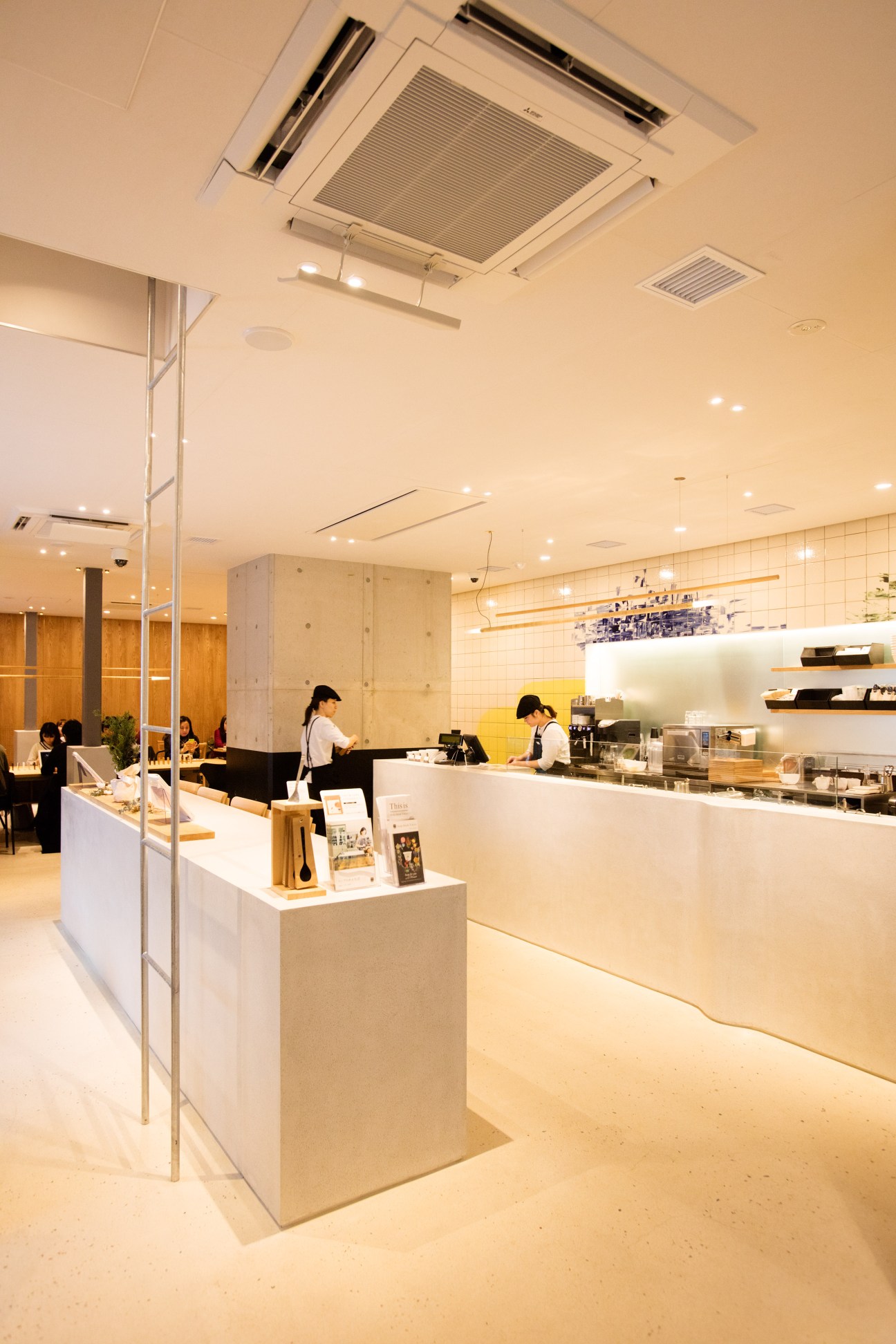 Interior of Soup Stock Tokyo restaurant with white counter, staff, and minimalist design under elevated tracks.
