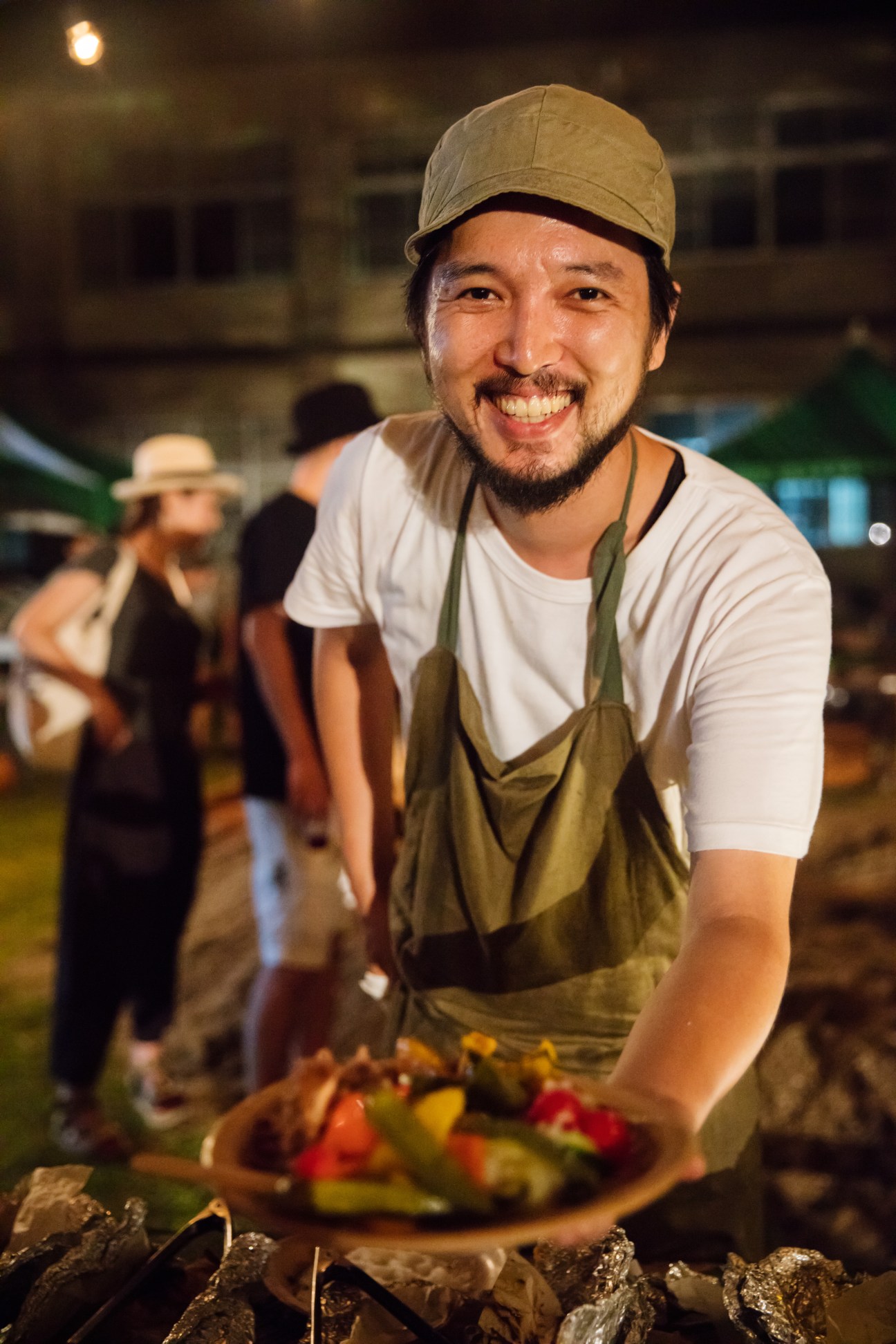 Chef Kenta Hayashi of Hay Grill & Coffee smiles at the camera while holding a plate of food at night.