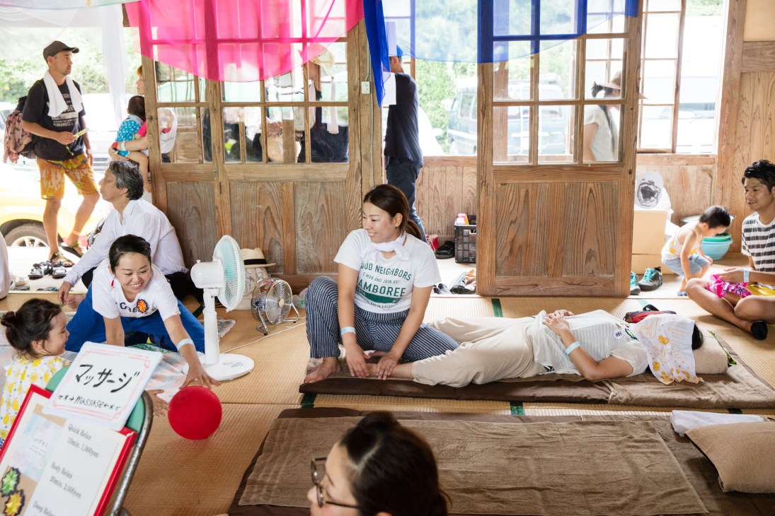 Masseur and hair stylists work with visitors inside the wooden schoolhouse during the Good Neighbors Jamboree.