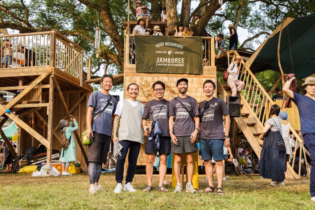 Founder Shuichiro Sakaguchi and four members of the jamboree's organising committee stand in front of a wooden treehouse structure at the Good Neighbors Jamboree.