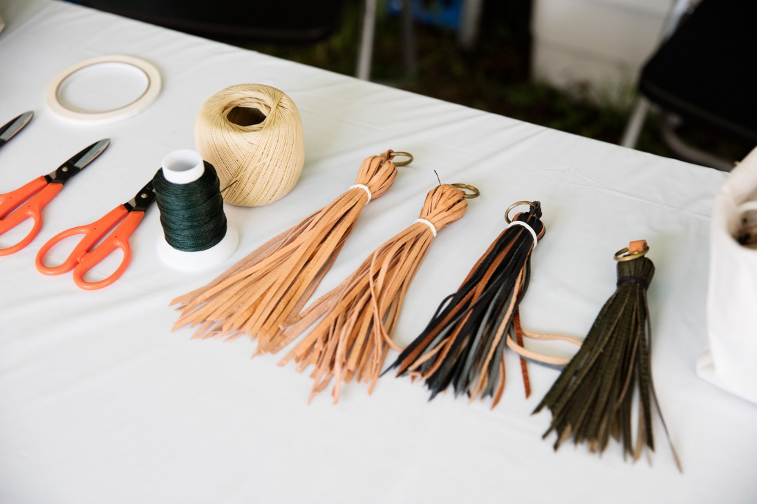Leather craft supplies displayed on white table including tassels, thread, scissors and natural fiber cord.