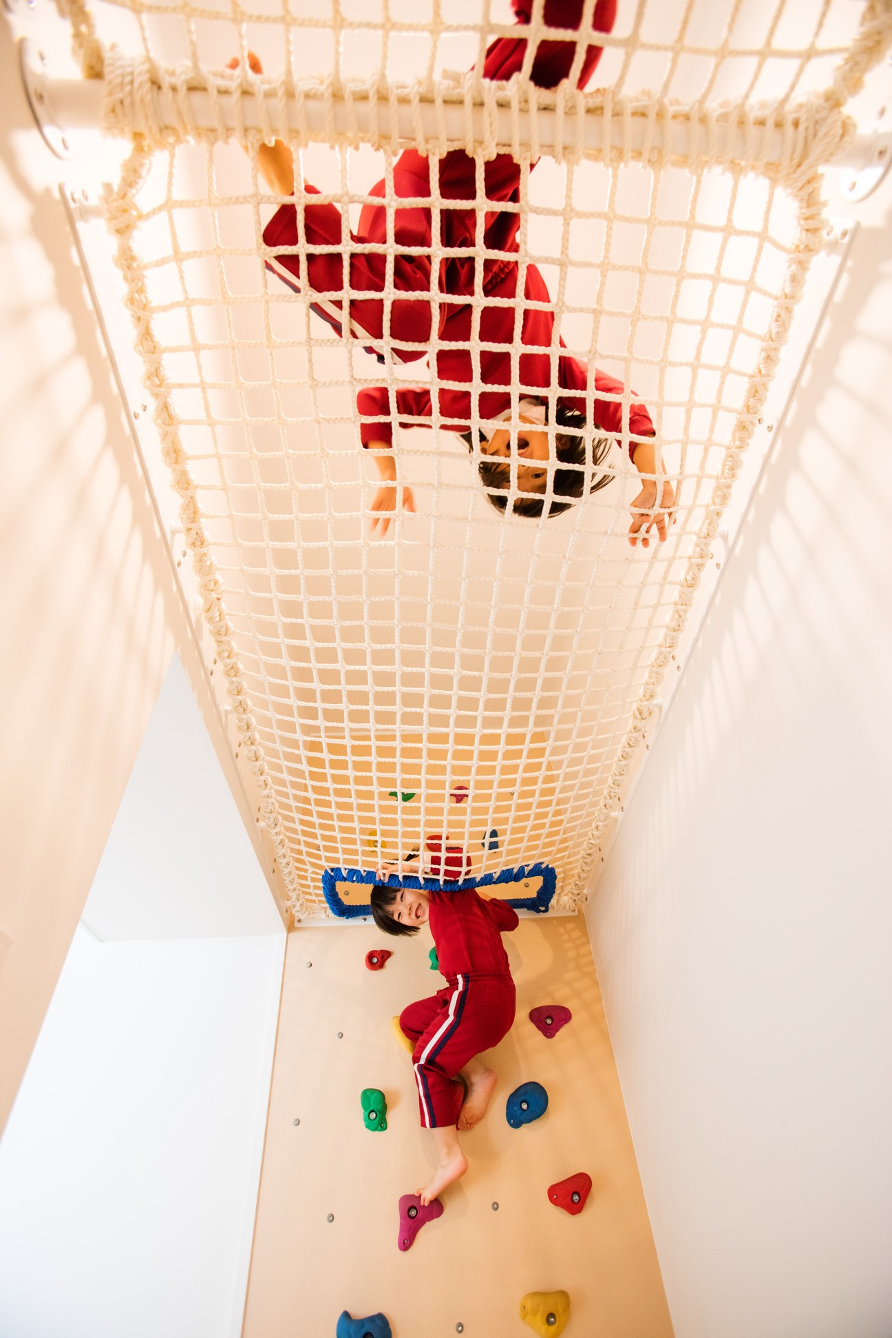 Child climbing on indoor climbing wall with colored holds and safety net at Obama Kodomoen kindergarten.