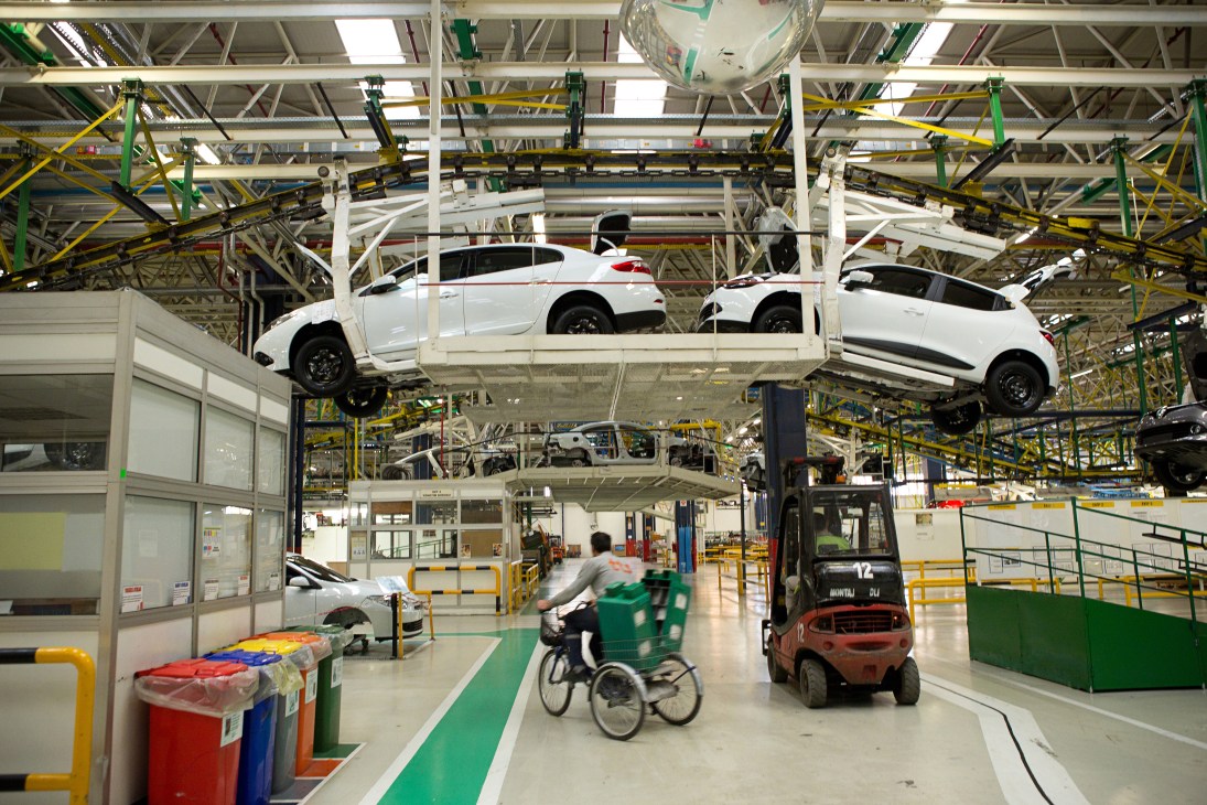 White cars suspended on conveyor system at Renault-Oyak production facility with industrial machinery overhead.
