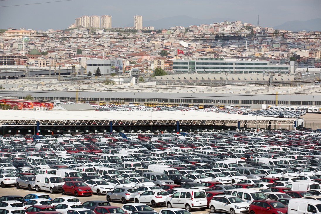 Aerial view of Renault-Oyak's sprawling Bursa facility with thousands of parked cars, industrial buildings, and city skyline beyond.