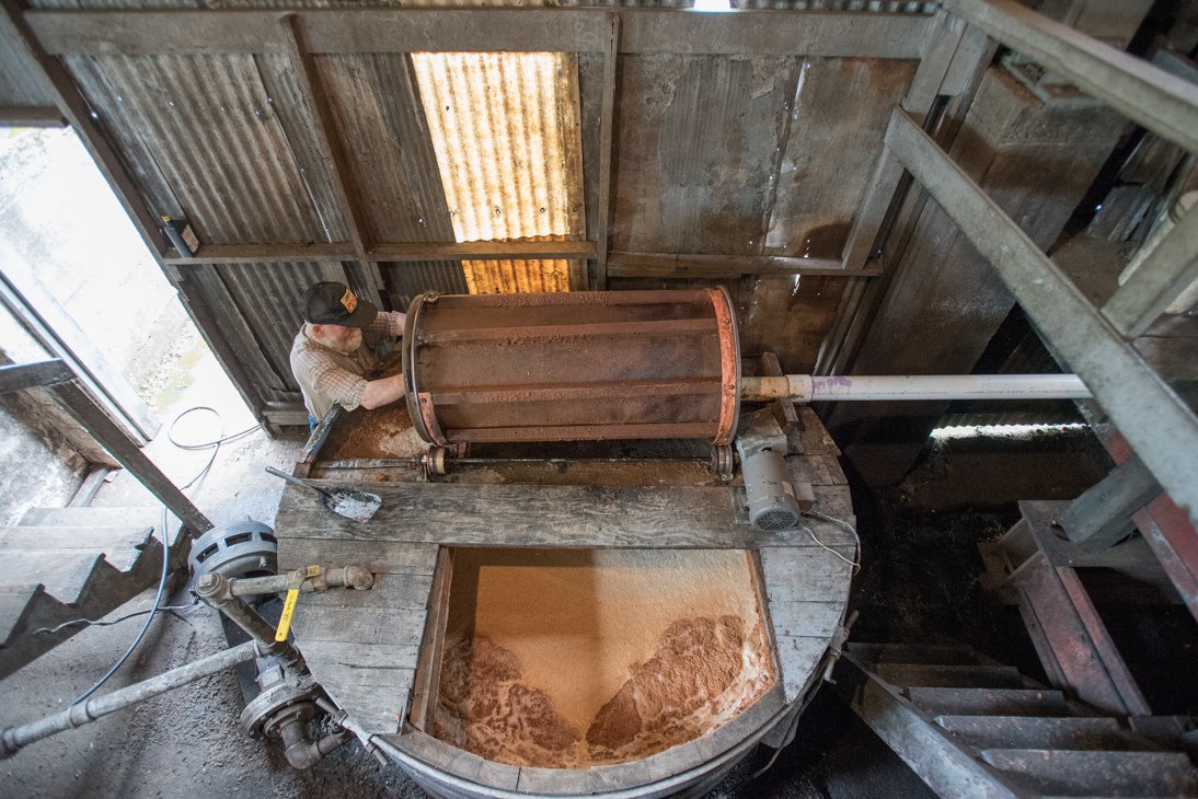 Worker operating a hydraulic accordion press to squeeze juice from chopped apples at the distillery.