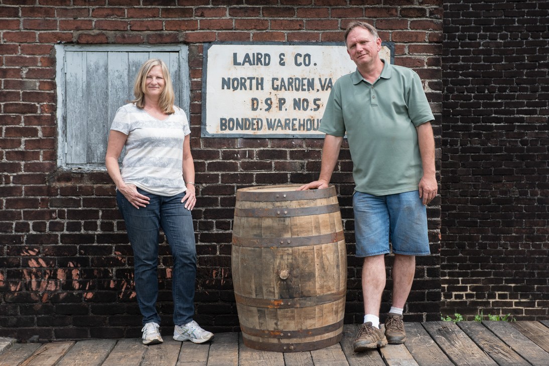 Lisa Laird Dunn and Danny Swanson stand beside a wooden barrel against a brick wall with a Laird & Co. sign.