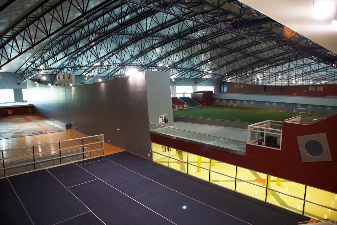 Interior of Aspire's multi-sport dome showing tennis courts and indoor football pitch with steel framework ceiling.