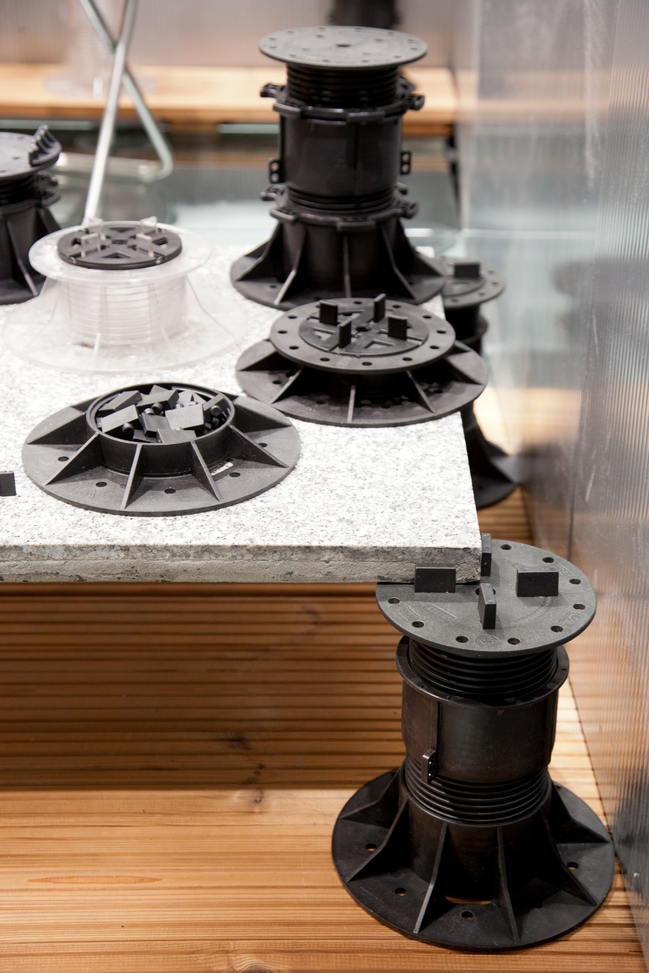 Adjustable paving pedestals in black and white displayed on a concrete surface with wooden flooring.