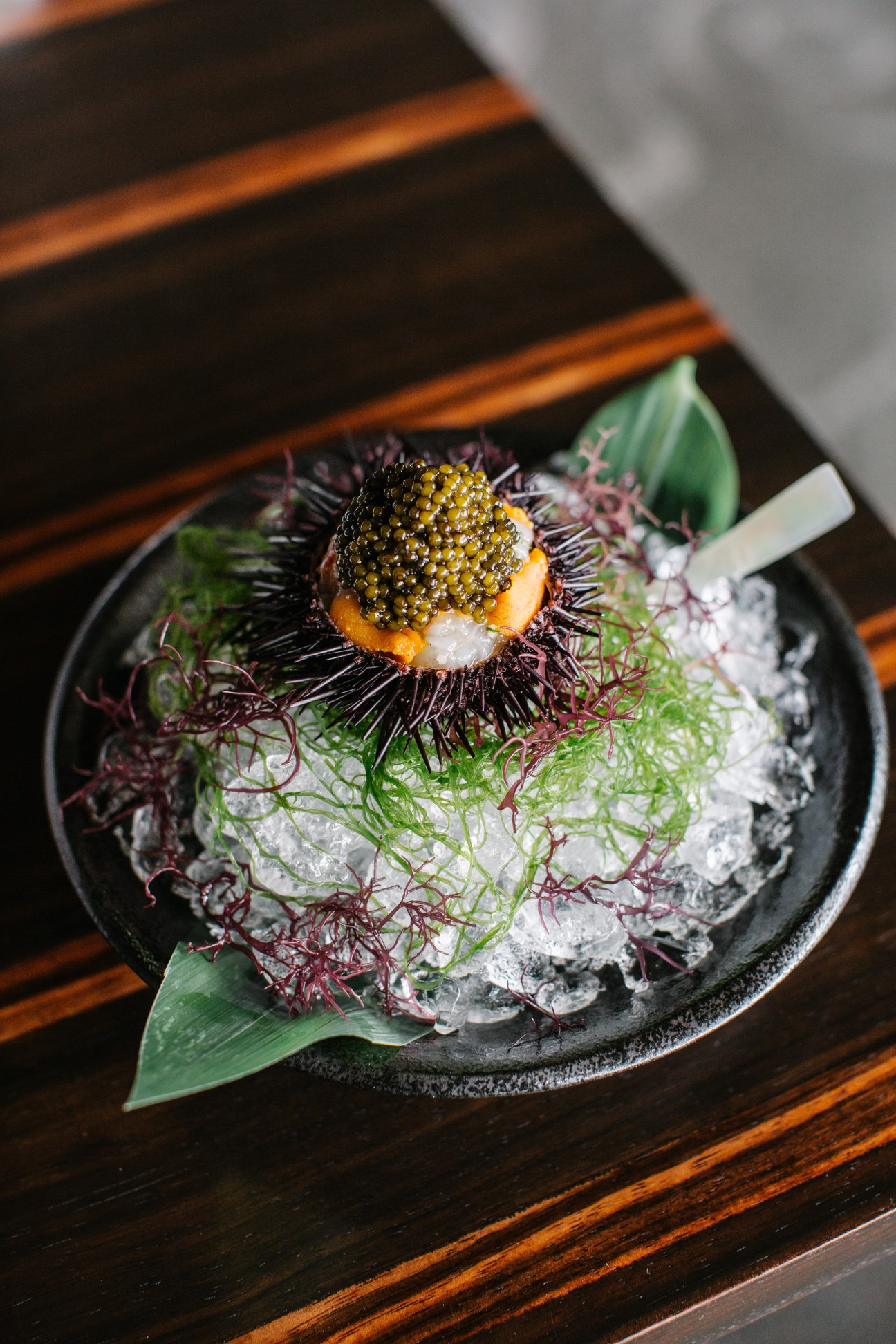 Marinated botan shrimp with sea urchin and oscietra caviar served on a black plate with microgreens and ice.