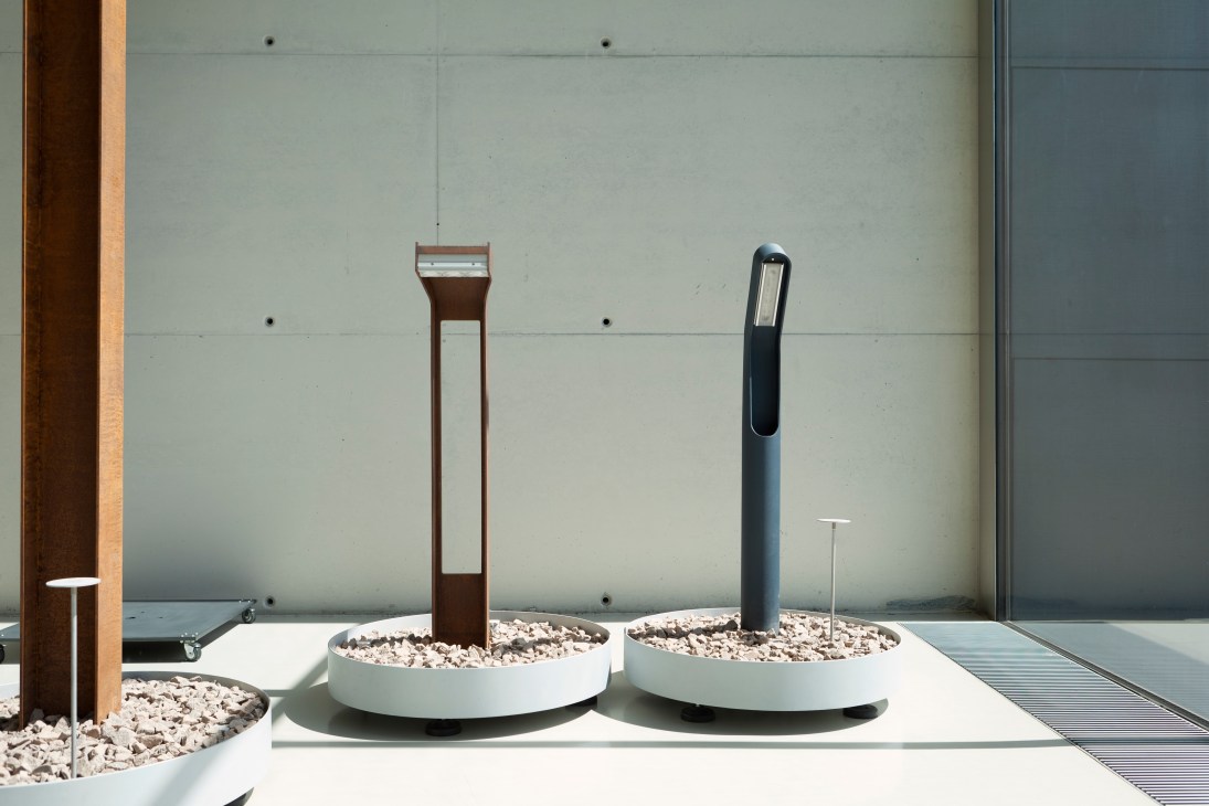 Ewo outdoor lighting prototypes displayed on white planters filled with gravel against a minimalist concrete wall.