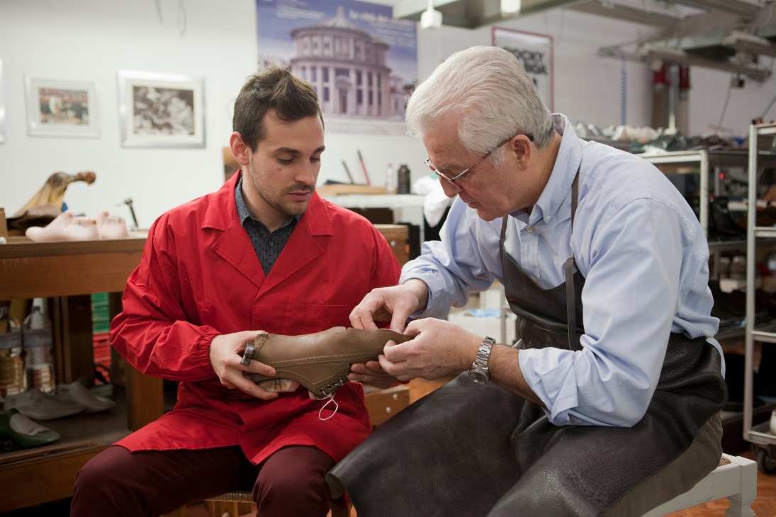 Master shoemaker Silvano Sollini instructs apprentice Matteo Valle on stretching leather over a wooden last at Santoni factory.