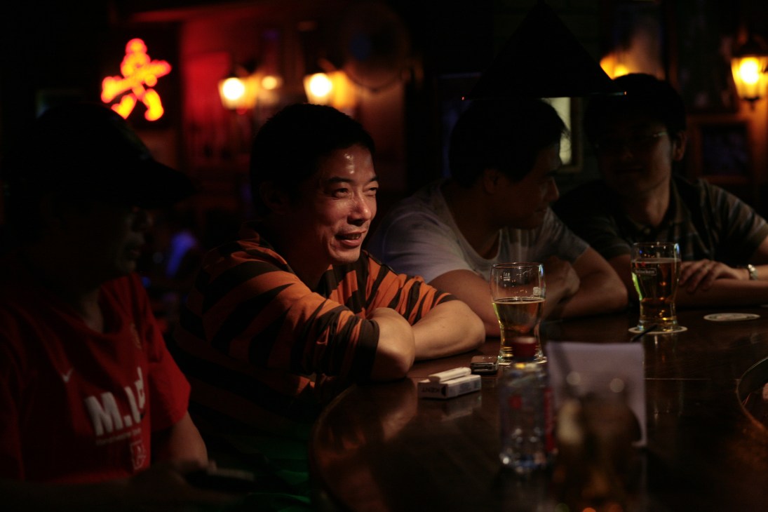 People socializing at a dimly lit bar with neon signs and drinks on the counter.