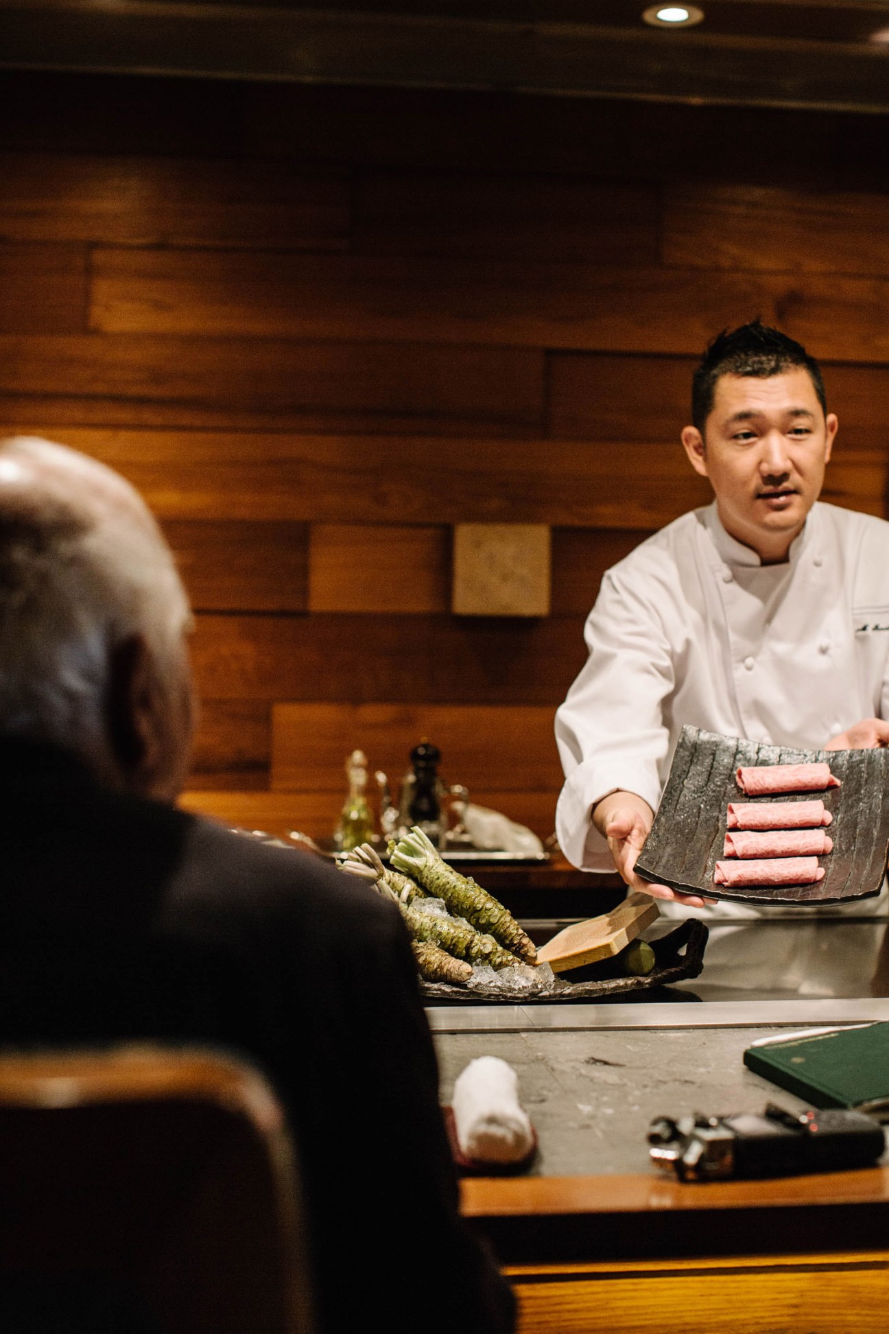 Chef Tetsuya Wakuda presents raw ingredients including seafood to a diner at the counter.