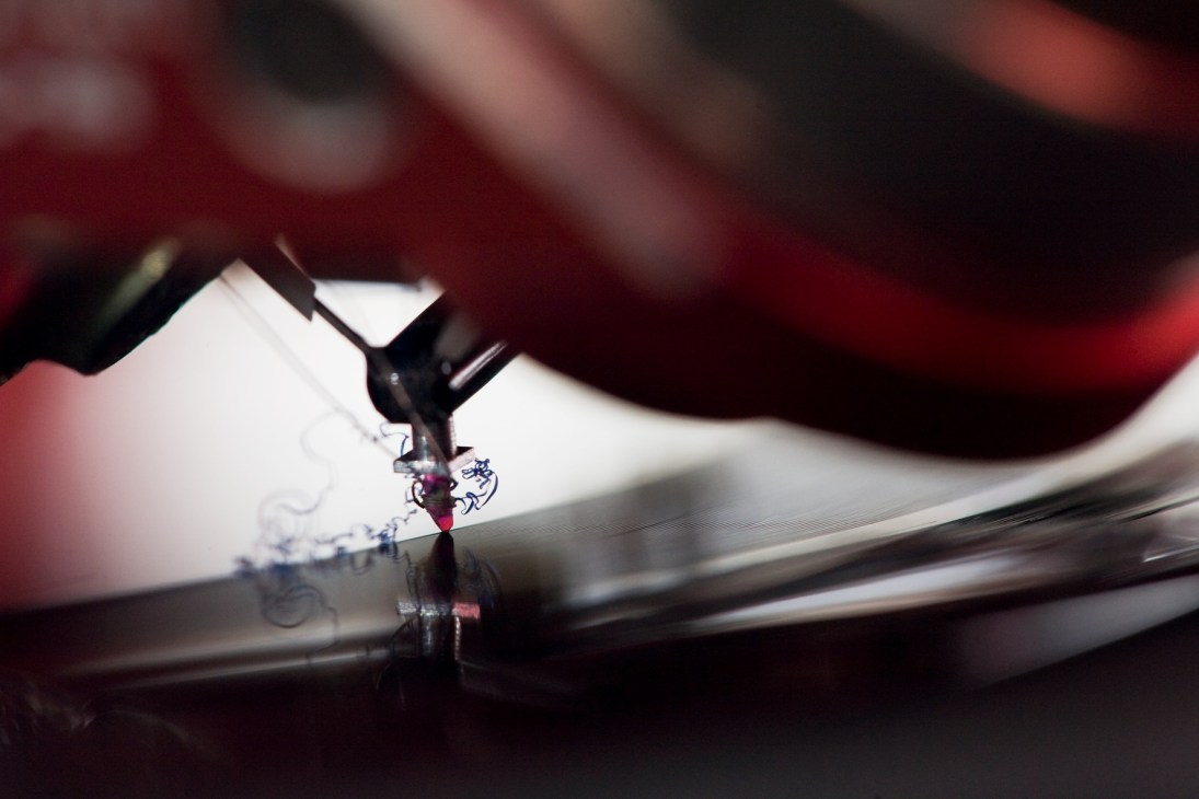 A cutting stylus engraving grooves into a white dub-plate during vinyl record production.