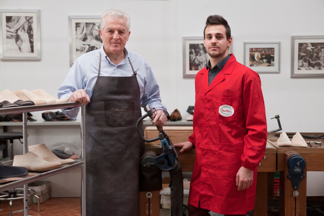 Master shoemaker Silvano Sollini and apprentice Matteo Valle stand together in a Santoni workshop surrounded by wooden shoe lasts.