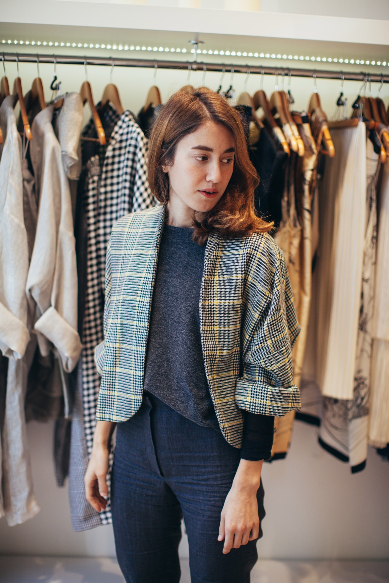 Fashion designer Timi Hayek wearing a patterned blazer in her boutique studio surrounded by hanging clothes.