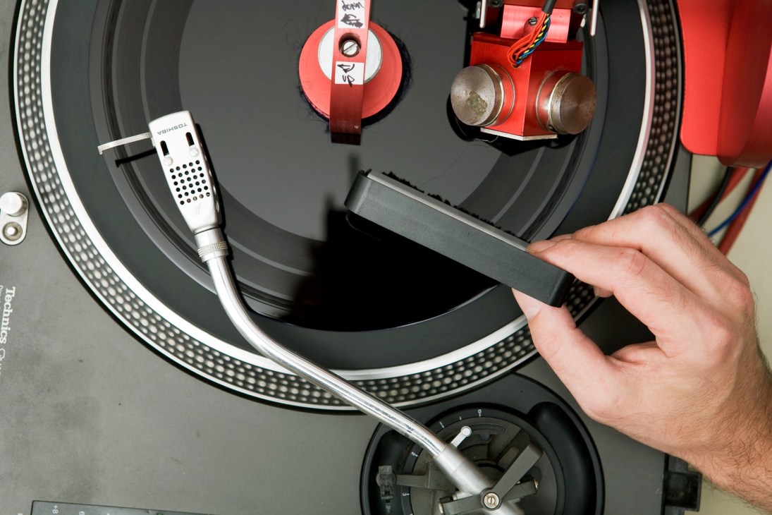Hand holding a stylus over a dub-plate cutter with red and black components on a turntable.