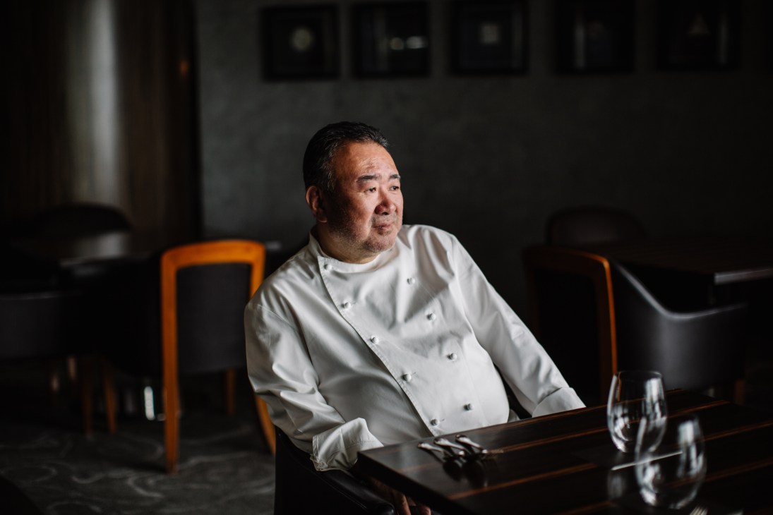 Chef Tetsuya Wakuda seated at counter in white chef's coat at Waku Ghin restaurant.