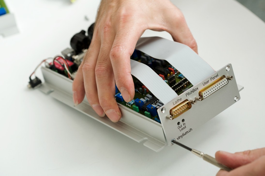 A hand assembles electronic components of a Vinylium cutting lathe computer with visible circuit boards and connectors.
