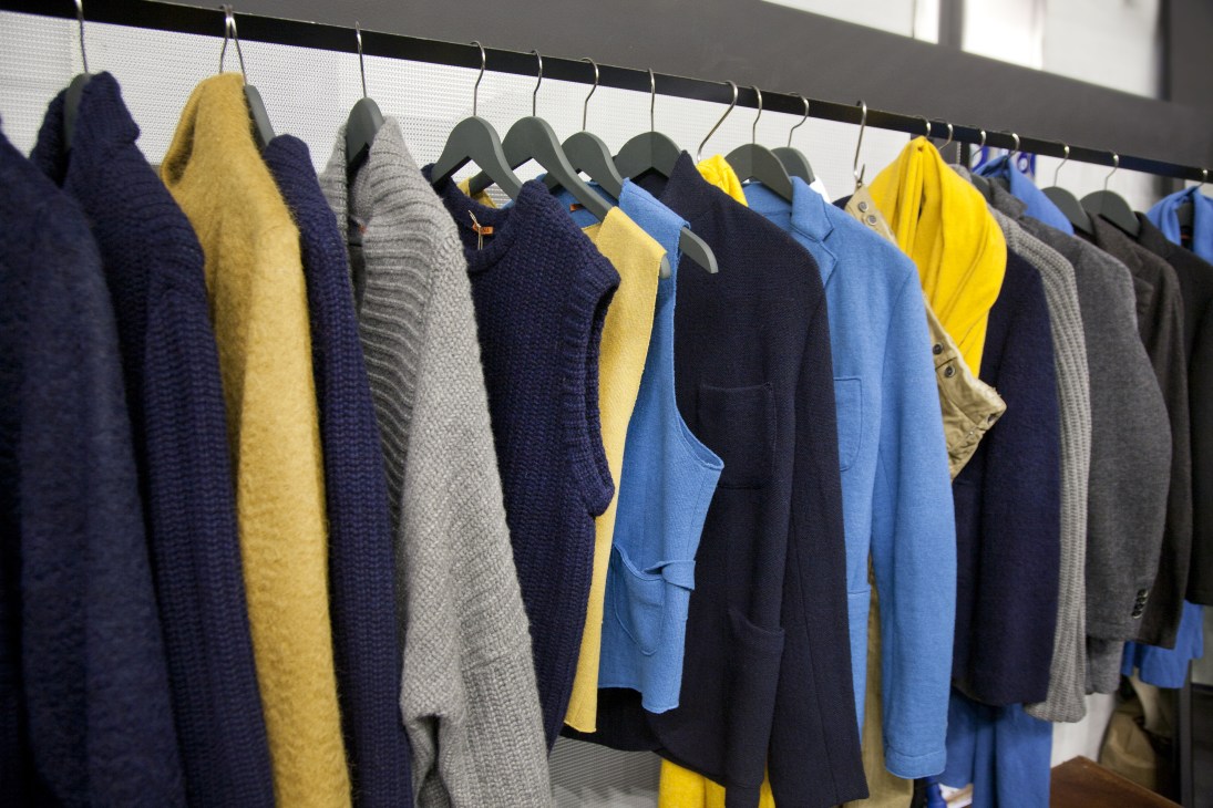 Colorful menswear garments displayed on hangers at Barena's booth, featuring blues, yellows, grays and navy tones.