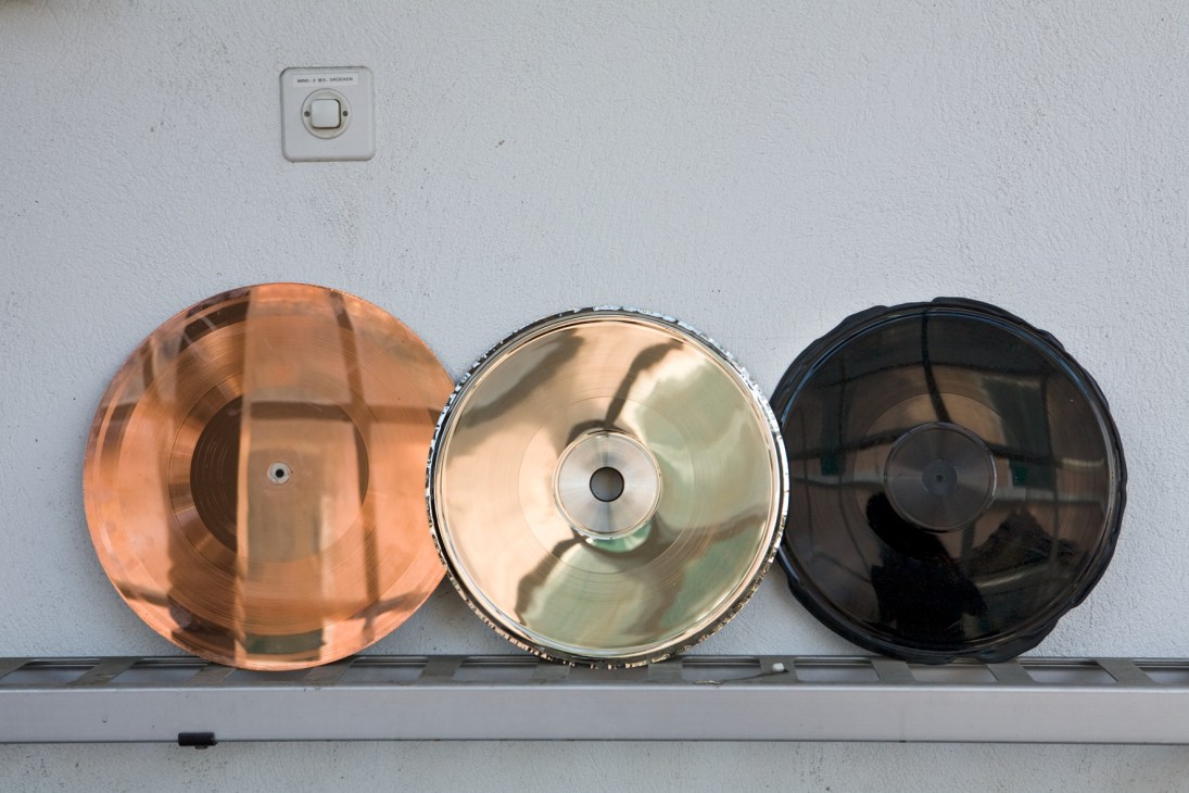 Three metal discs in copper, silver, and black showing various stages of vinyl record production.