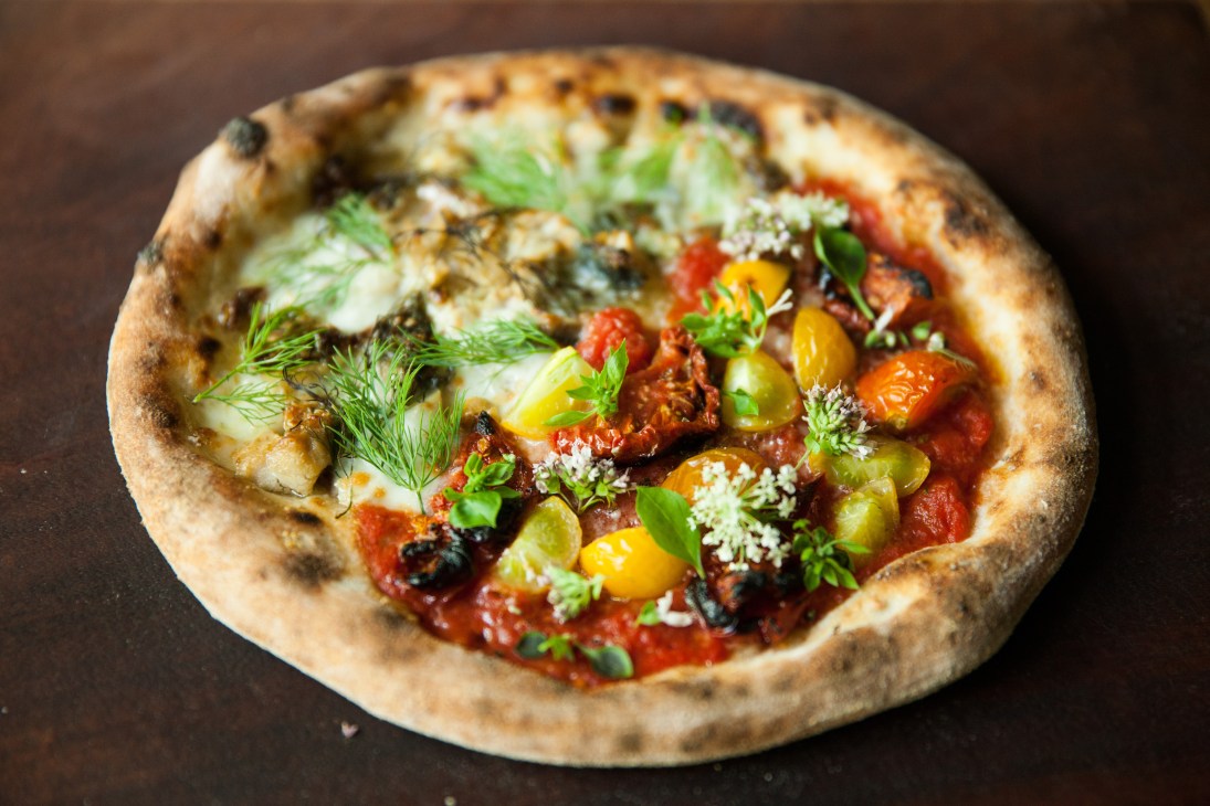 Wood-fired pizza topped with cheese, vegetables, and fresh herbs at Monk restaurant in Kyoto.