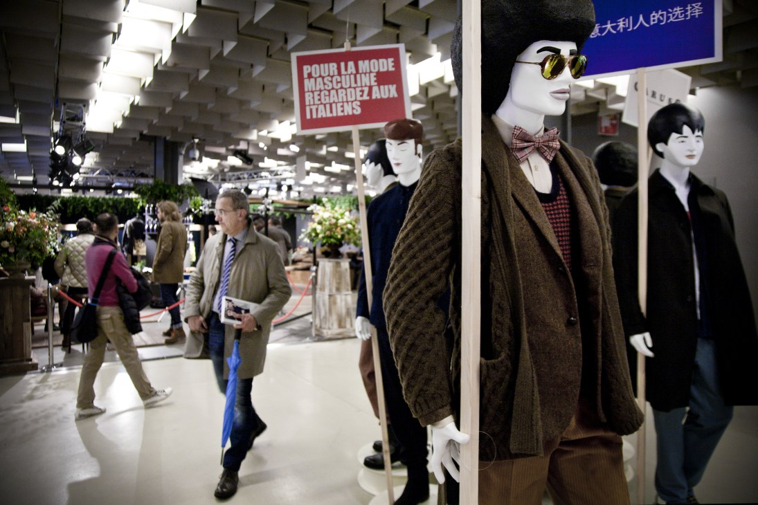 Mannequins wearing brown outerwear at Caruso's booth with a French-language sign at Pitti Uomo menswear show.