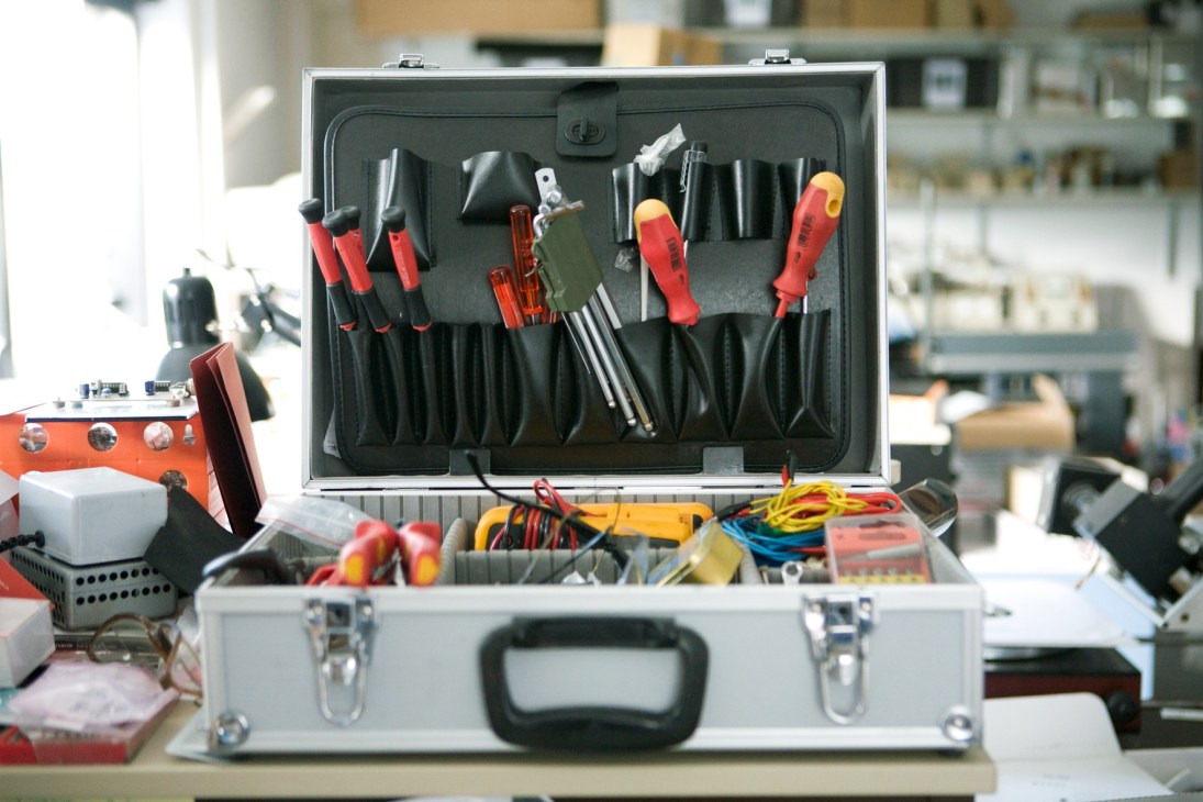 An open toolbox containing organized hand tools with red handles and various metal instruments in a workshop.