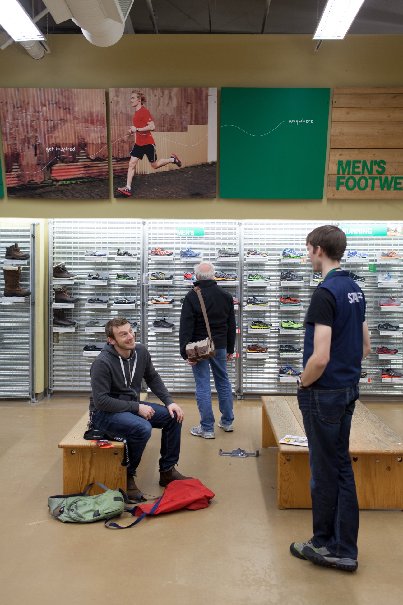 MEC store employee providing advice to customers in the shoe department with display wall behind them.