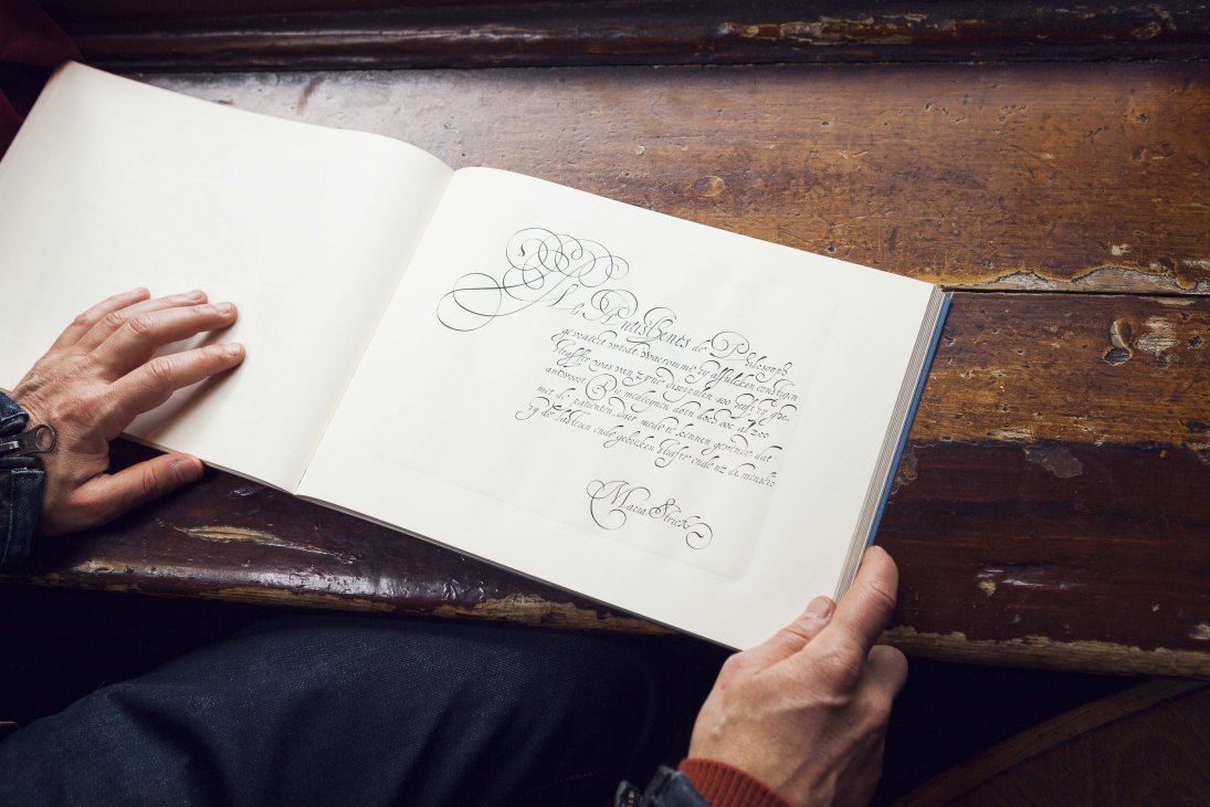 Person holding open a book displaying handwritten cursive calligraphy on white pages.