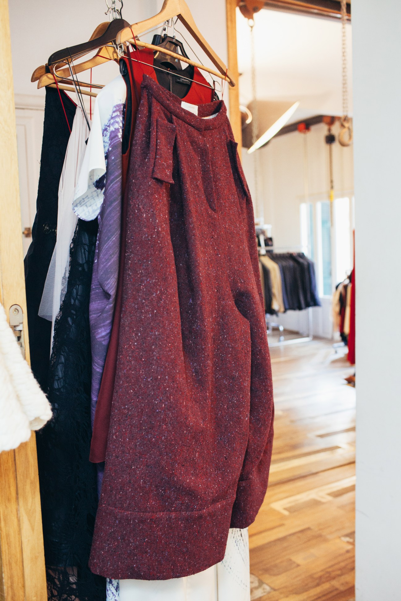 Burgundy draped dress on wooden hanger in design studio with other garments visible