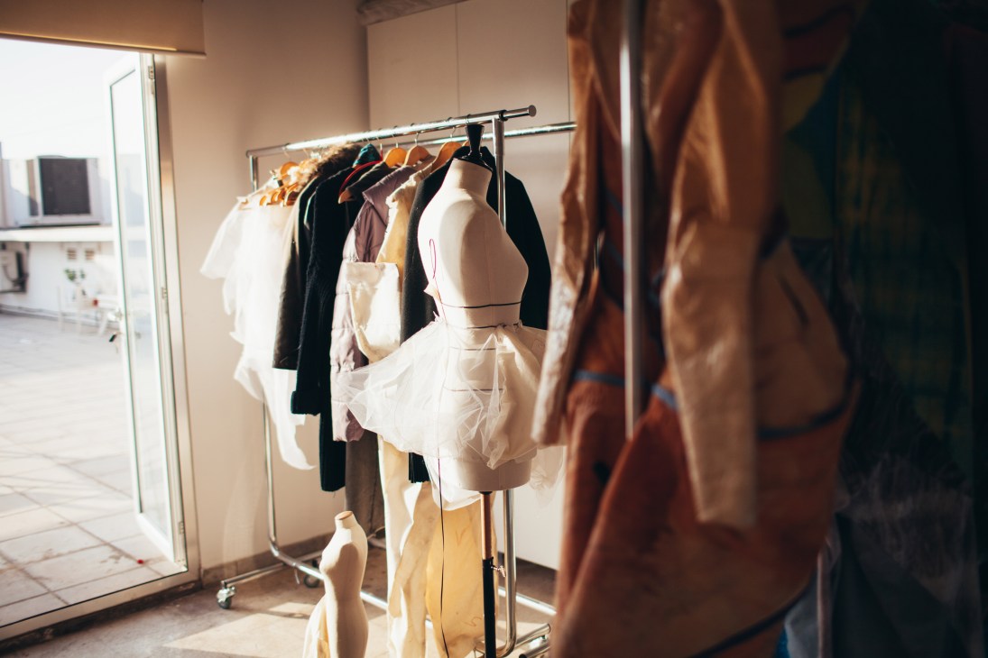 Fashion designs displayed on a rack and dress form in a bright studio space.
