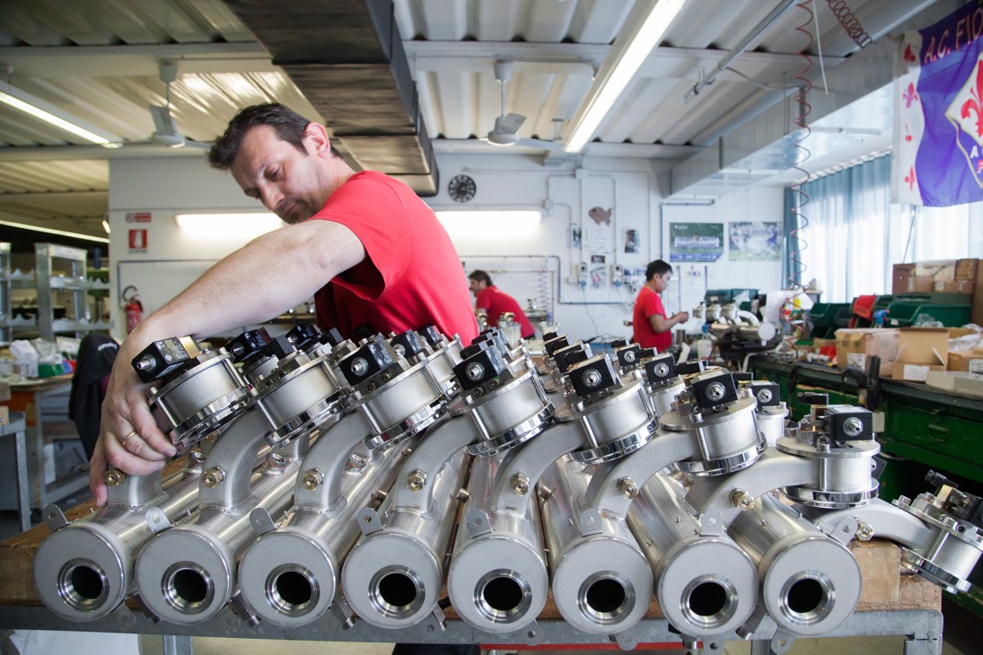 Worker in red shirt assembling espresso machine boilers at La Marzocco factory.