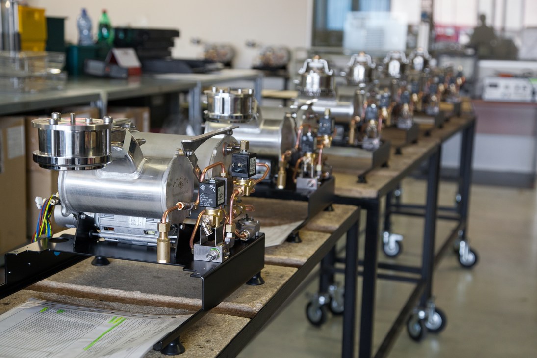 Espresso machine components assembly line with boilers and hydraulic parts on production carts.