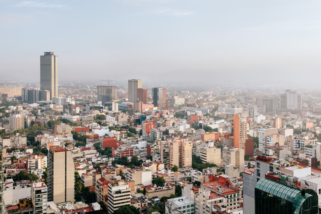 Aerial view of Mexico City's sprawling urban landscape with high-rise buildings, residential areas, and smog.
