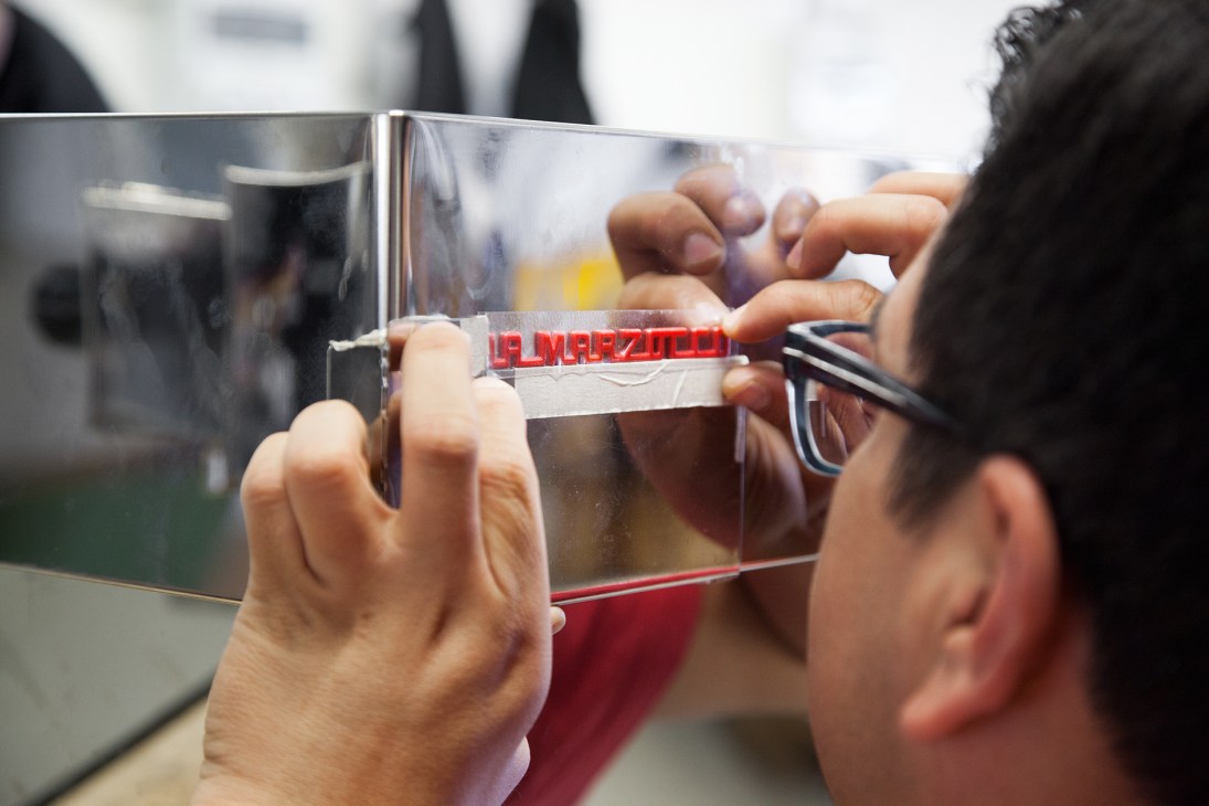 Worker applying the red La Marzocco logo to a stainless steel espresso machine component.