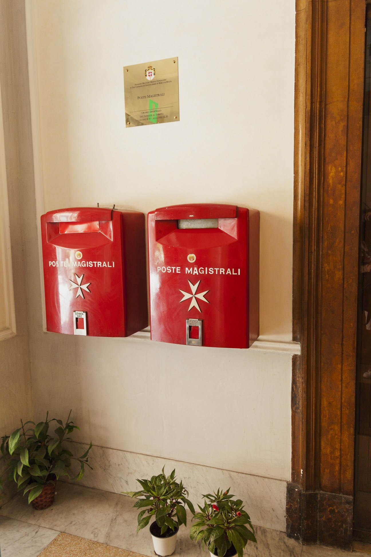 Two red Poste Magistrali postboxes mounted on a white wall with a brass plaque above them.