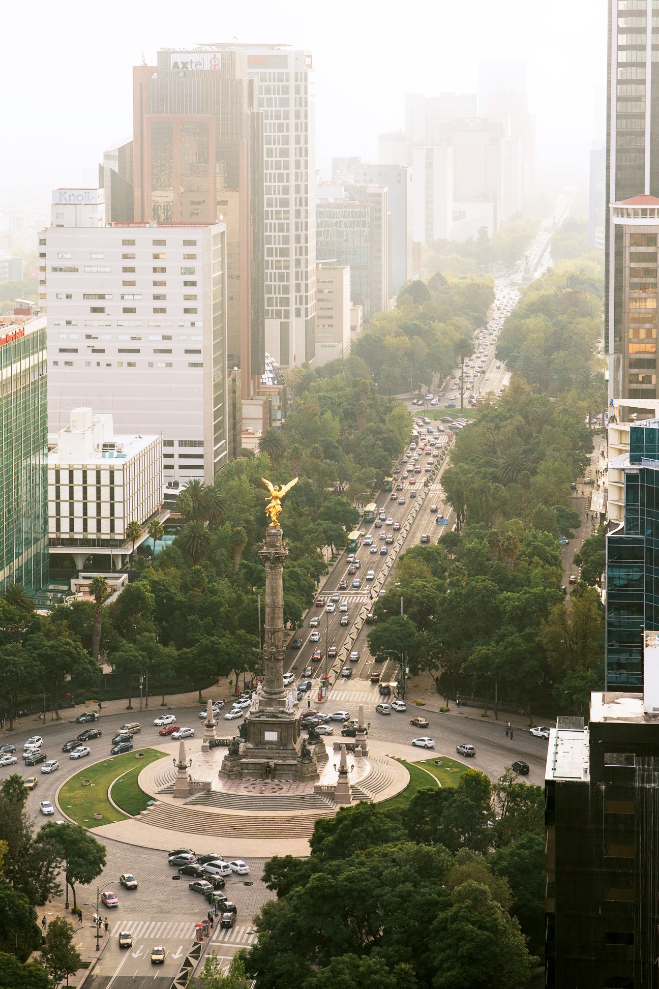 Aerial view of Angel of Independence monument on Paseo de la Reforma with traffic and tree-lined avenue below.