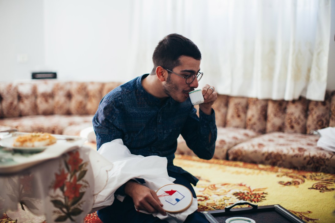 Salim Azzam drinks from a cup while holding embroidered fabric in a traditional Lebanese interior.