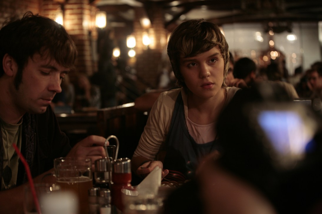 Masha Netrebenko and her boyfriend Zhenya sit at a bar with drinks in a dimly lit venue.