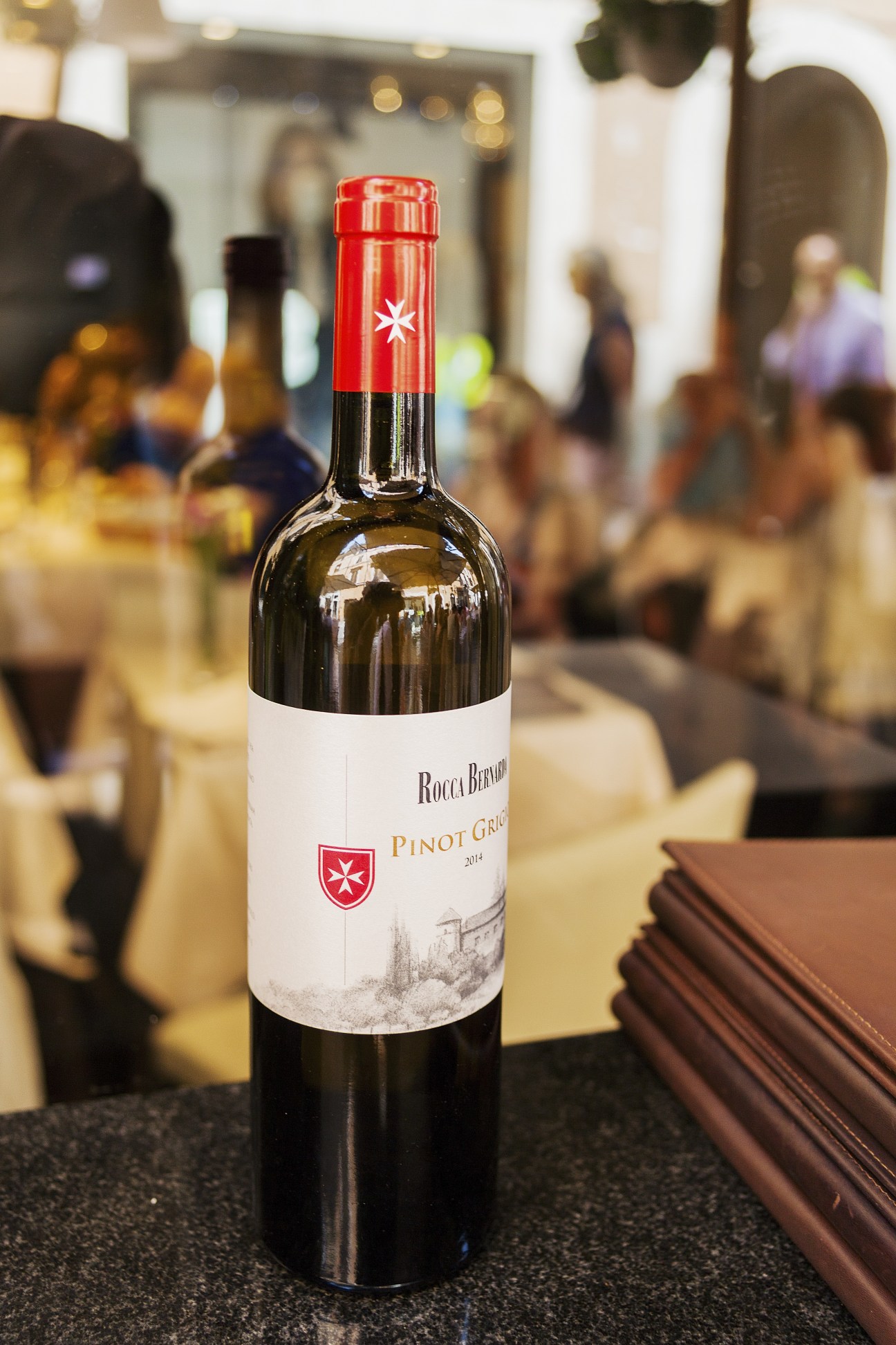 Bottle of Rocca Bernarda Pinot Grigio wine with red foil cap and white label featuring a Maltese cross emblem.