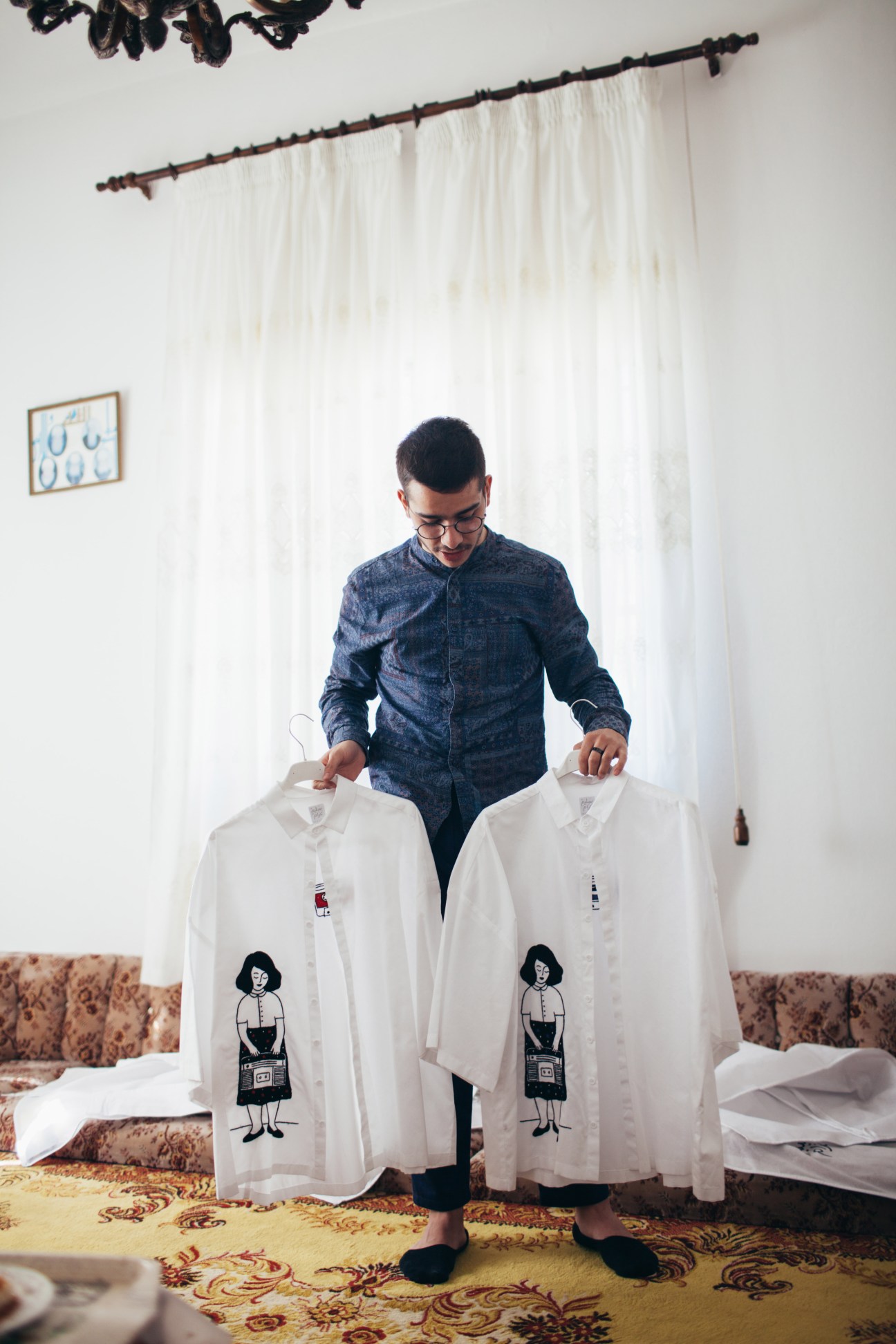 Man in denim shirt holds two white button-up shirts with illustrated female figures printed on them.