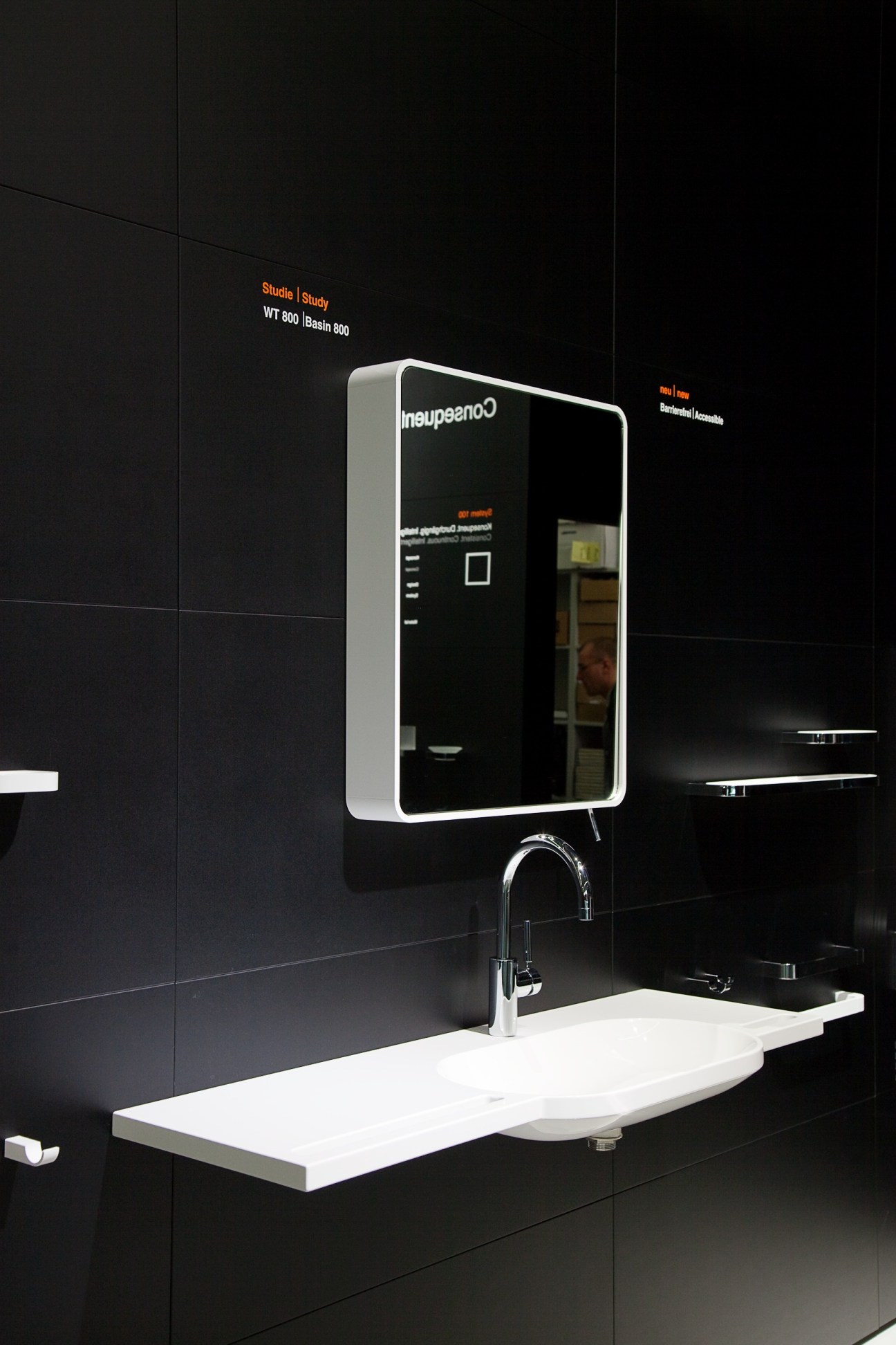 System 800 by Hewi bathroom installation with white basin, chrome tap, and illuminated mirror cabinet against black tiled wall.