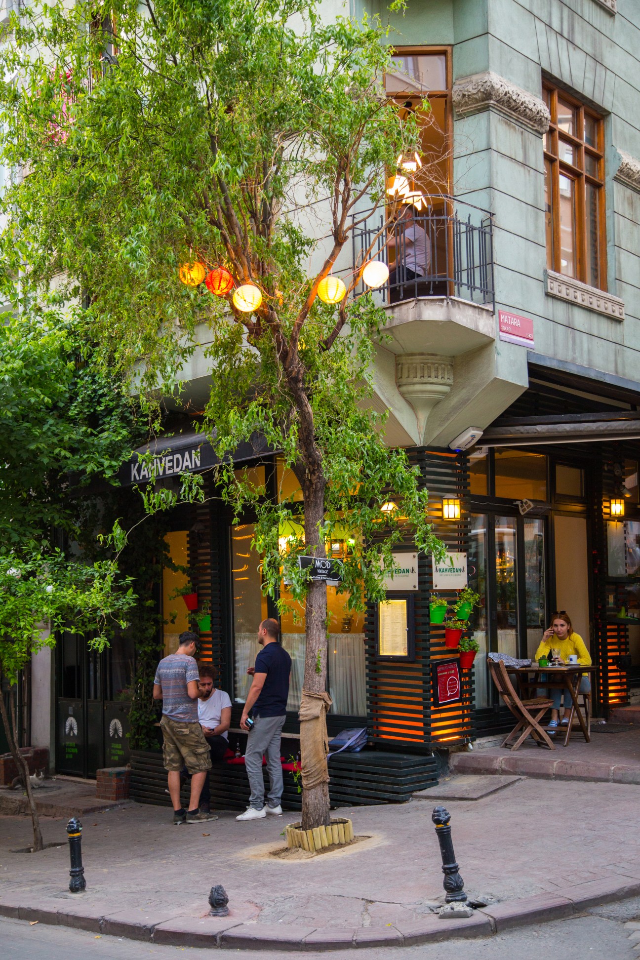 Café-lined Akarsu Caddesi street in Istanbul with large tree and yellow lanterns.